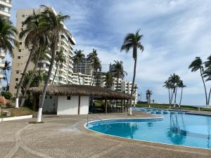 a swimming pool with palm trees and a building at Mayan Playa Departamento Uxmal in Acapulco