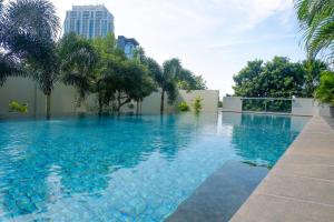 a swimming pool with blue water and palm trees at Spacious and Restful 2BR at Sumatra36 Apartment By Travelio in Surabaya