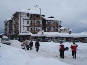 personnes marchant dans la neige devant un bâtiment dans l'établissement Hotel Dumanov, à Bansko