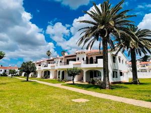 a large white building with palm trees in front of it at Apartamento Trini en Son Bou, frente al mar, perfecto para vacaciones in Alaior