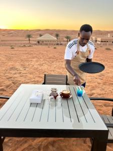 a man standing next to a table in the desert at Desert Gate Resort in Al Raka