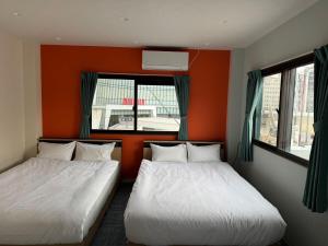two beds in a room with orange walls and windows at Guest House新今宫 in Osaka