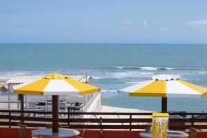 two tables with yellow and white umbrellas next to the ocean at Pipas Ocean by Pipa Centro in Pipa