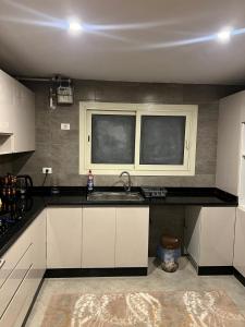 a kitchen with white cabinets and a sink and two windows at شقة فندقية نيو جيزة الشيخ زايد in Abū Rawwāsh