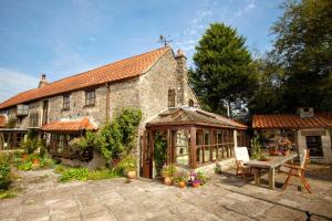an old stone house with a greenhouse in the yard at Spindle Cottage Holidays in Radstock