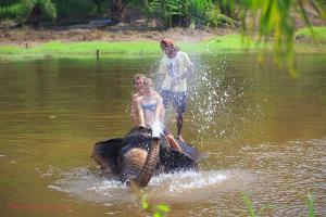 dos personas montadas en la espalda de un elefante en el agua en Baan Rim Tarn B&B, en Takua Pa