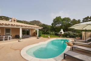 a swimming pool with an umbrella and a house at Villa Corallo in Costa Rei