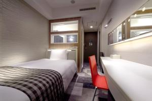 a hotel room with a bed and a red chair at Sotetsu Fresa Inn Shimbashi-Karasumoriguchi in Tokyo