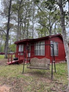 a red cabin in the woods with a swing at Guest House in Hemphill