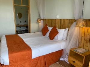 a bedroom with a large bed with white sheets and orange pillows at Acacia Wilderness Mweya in Kasese