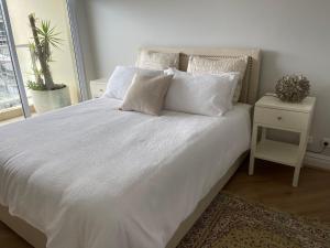 a white bed with white pillows and a night stand at Coastal luxury in Sydney
