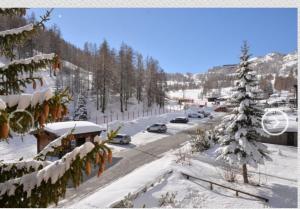 une rue couverte de neige avec des voitures garées sur la route dans l'établissement House La Motta, à Borgata Sestriere