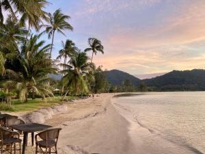 a beach with chairs and palm trees next to the water at Siam Royal View Pool Villa in Ko Chang