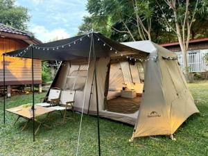 a tent in the grass with two chairs and a table at Rim Haad Villa and Camping Space in Ban Tanjong In