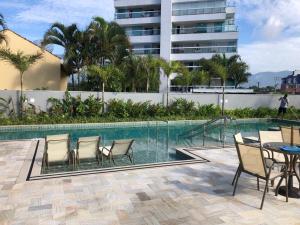 a swimming pool with chairs and a table next to a building at Apto de ferias em Bertioga Maitinga in Bertioga