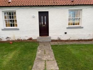 a white house with a black door and windows at Papa Jim's Cottage in Dirleton