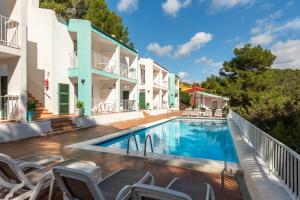 a swimming pool with chairs next to a building at Apartamentos alta galdana playa in Cala Galdana