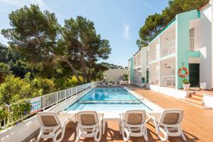 an image of a swimming pool with chairs and a house at Apartamentos alta galdana playa in Cala Galdana