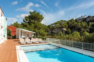 a swimming pool with chairs next to a house at Apartamentos alta galdana playa in Cala Galdana +10 photos