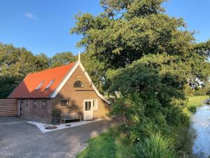 a barn with an orange roof next to a river at Boerderijhuisje 22 - Landelijk logeren bij Sneek in Loënga