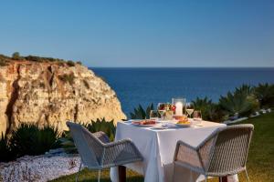 a table with a white tablecloth and chairs and the ocean at Tivoli Carvoeiro in Carvoeiro +37 photos