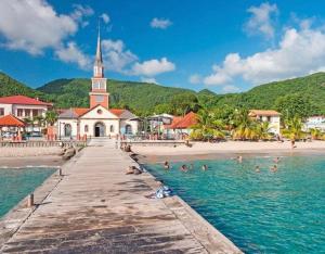a beach with people in the water and a church at Séjour Authentique et Paisible in Les Anses-dʼArlets