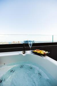 a bath tub with a glass of wine and a plate of fruit at SO City Hotel Adults Only in St. Julianʼs