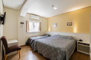 a bedroom with a bed and a chair and a window at Hotel Erechim in Porto Alegre
