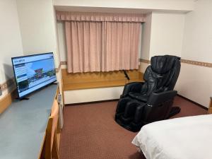 a room with a bed and a chair and a television at Hotel Alpha-One Hofu in Hofu
