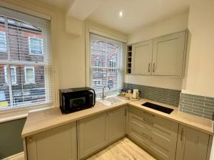 a kitchen with white cabinets and a sink and two windows at A3 High Town Apartments, steps from Luton train station in Luton