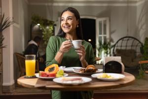 a woman holding a cup of coffee at a table with breakfast at Pousada Vale Valparaíso Inn- Polo gastronômico in Petrópolis