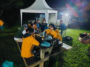 a group of people sitting at a picnic table at night at D'Sentra Camping Ground in Pengalengan