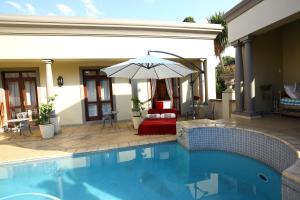 a swimming pool with an umbrella next to a house at Villa Lugano Guesthouse in Johannesburg