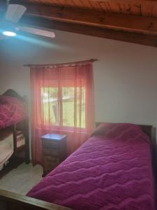 ein Schlafzimmer mit einem lila Bett und einem Fenster in der Unterkunft Cabañas Cuncumen in Los Reartes
