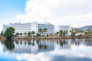 duży biały budynek z palmami przed jeziorem w obiekcie Eix Lagotel Holiday Resort w Playa de Muro