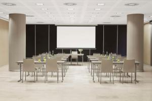 a conference room with tables and chairs and a white screen at NH Alicante in Alicante