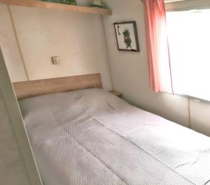 Una cama en una habitación pequeña con ventana. en Bungalow charmant à Saint-Pierre-d'Oléron avec jardin clôturé, en Saint-Pierre-dʼOléron