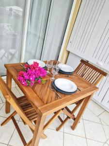 ein Holztisch mit Tellern, Gläsern und Blumen darauf in der Unterkunft Charmant appartement à La Trinité avec piscine partagée - 40 m² in La Trinité