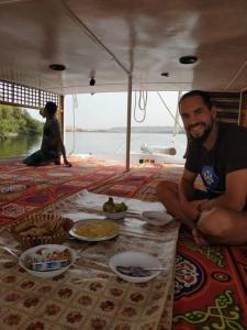 a man sitting on a boat with food on the floor at Mama Africa Felucca in Aswan