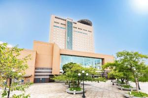 Un edificio alto con árboles delante. en ART HOTEL Kashima Central, en Kamisu