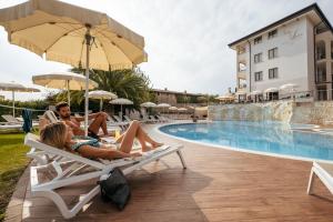 a group of people sitting on chairs next to a swimming pool at Villa Luisa Resort & Luxury Apartments in San Felice del Benaco