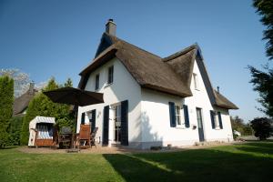 a white house with a table and an umbrella at Reetdachhaus - Reet am See in Börgerende-Rethwisch