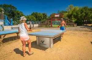 a woman standing at a ping pong table in a park at ZEcamping animé dog friendly familial piscine couverte in Saint-Georges-dʼOléron