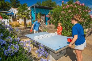 a woman and two children standing around a ping pong table at ZEcamping animé piscine couverte club enfant animations dog friendly in La Faute-sur-Mer