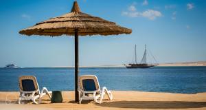 dos sillas y una sombrilla en una playa con un barco en Al Dora Residence Suites Hurghada, en Hurghada