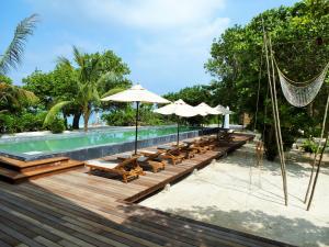 einen Pool mit Stühlen und Sonnenschirmen neben einem Resort in der Unterkunft The Barefoot Eco Hotel in Hanimaadhoo