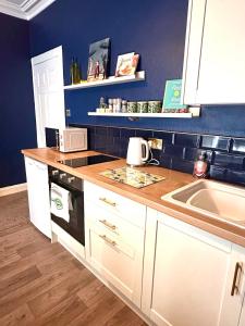 a kitchen with white cabinets and a sink and blue walls at Small Cosy Flat in Helensburgh +8 photos