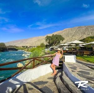 a woman in a pink dress leaning on a fence next to a river at Hotel Rustica Lunahuana in Uchupampa +10 photos