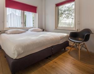 a bed in a room with a chair and two windows at Appartementen Domburg in Domburg