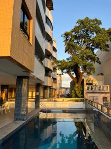 a swimming pool in front of a building with a tree at Apartamento Solar Rio Vermelho in Salvador